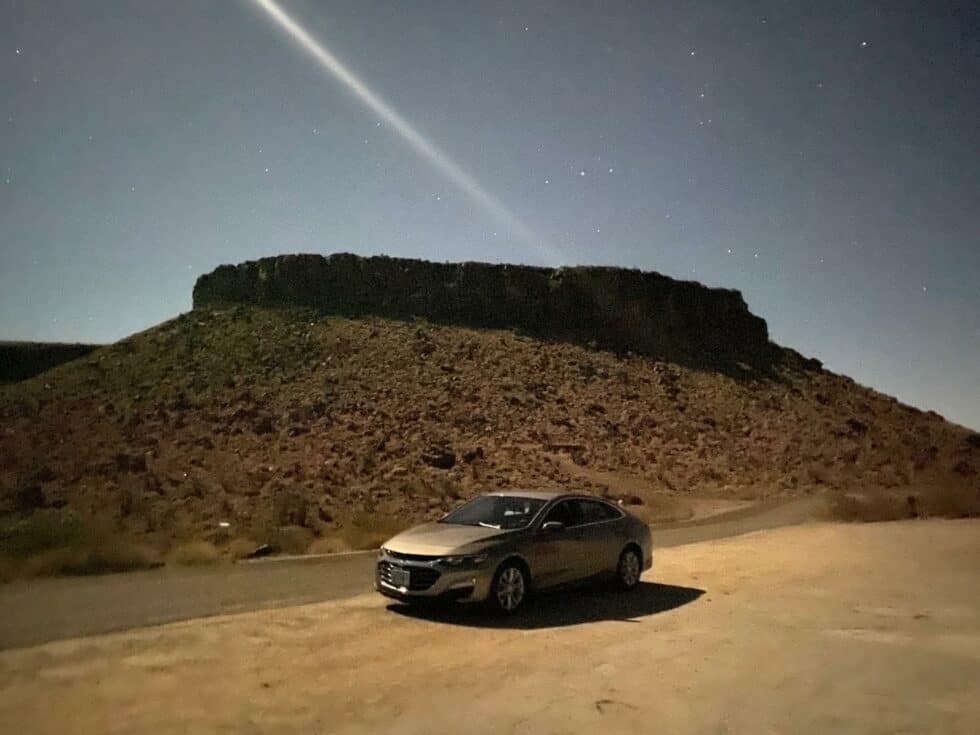 Voiture noire sous un ciel étoilé avec une montagne rocheuse en arrière-plan